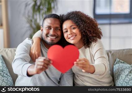 love, valentines day and relationships concept - happy african american couple holding red heart together at home. happy african american couple with heart at home
