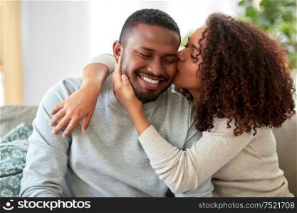 love, valentines day and relationships concept - happy african american couple sitting on sofa at home and kissing. happy african american couple kissing at home