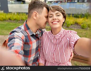 love, valentines day and relationships concept - happy couple in summer park taking selfie outdoors. happy couple in park taking selfie outdoors