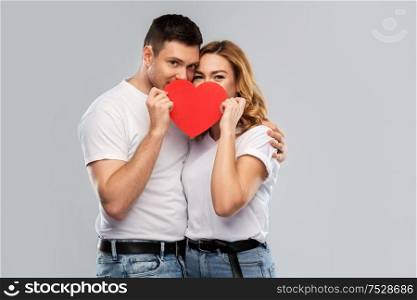 love, valentines day and relationships concept - smiling couple hiding behind big red heart over grey background. smiling couple hiding behind big red heart