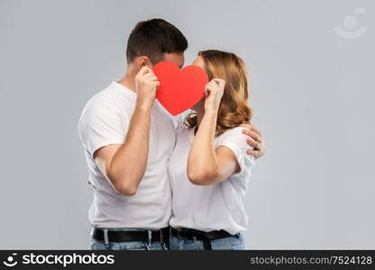 love, valentines day and relationships concept - smiling couple kissing behind big red heart over grey background. smiling couple kissing behind big red heart