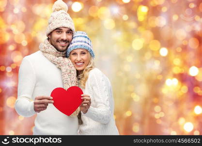 love, valentines day, couple, christmas and people concept - smiling man and woman in winter hats and scarf holding red paper heart shape over lights background