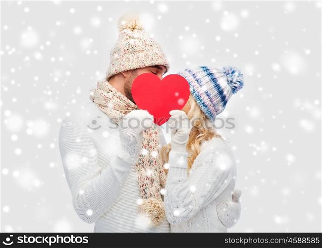 love, valentines day, couple, christmas and people concept - smiling man and woman in winter hats and scarf hiding behind red paper heart shape