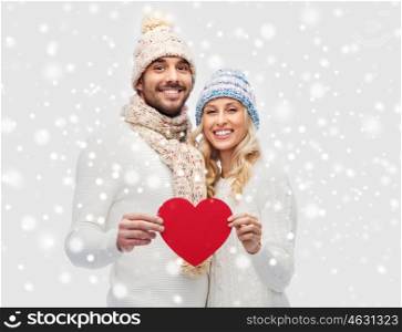 love, valentines day, couple, christmas and people concept - smiling man and woman in winter hats and scarf holding red paper heart shape