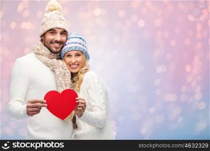 love, valentines day, couple, christmas and people concept - smiling man and woman in winter hats and scarf holding red paper heart shape over rose quartz and serenity lights background