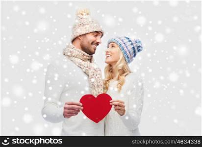 love, valentines day, couple, christmas and people concept - smiling man and woman in winter hats and scarf holding red paper heart shape