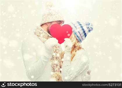 love, valentines day, couple, christmas and people concept - smiling man and woman in winter hats and scarf hiding behind red paper heart shape. smiling couple in winter clothes with red heart