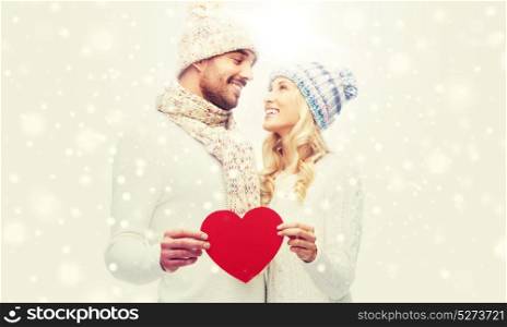 love, valentines day, couple, christmas and people concept - smiling man and woman in winter hats and scarf holding red paper heart shape. smiling couple in winter clothes with red heart