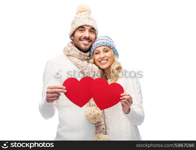 love, valentines day, couple, christmas and people concept - smiling man and woman in winter hats and scarf holding red paper heart shapes