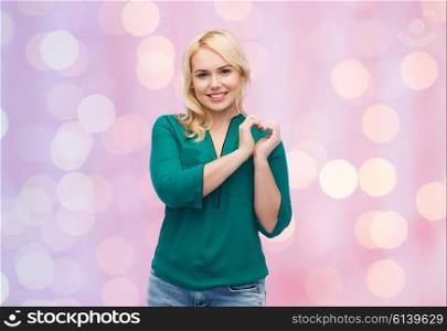 love, valentines day, gesture, plus size and people concept - smiling young woman in shirt and jeans showing heart shape hand sign over pink holidays lights background