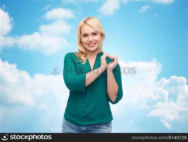 love, valentines day, gesture, plus size and people concept - smiling young woman in shirt and jeans showing heart shape hand sign over blue sky and clouds background