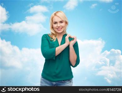 love, valentines day, gesture, plus size and people concept - smiling young woman in shirt and jeans showing heart shape hand sign over blue sky and clouds background