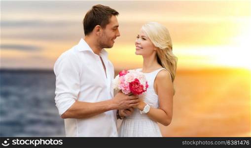love, wedding and people concept - happy couple in white clothes with flowers over sea background. happy couple with flowers over sea background