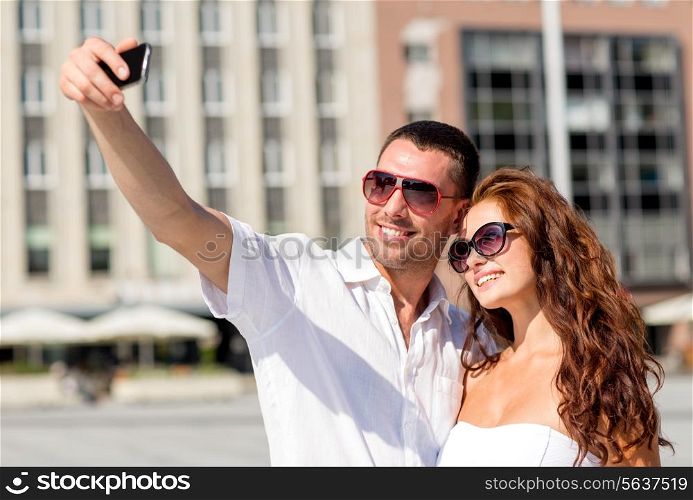 love, wedding, summer, dating and people concept - smiling couple wearing sunglasses making selfie with smartphone in city