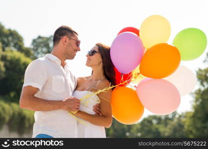 love, wedding, summer, dating and people concept - smiling couple wearing sunglasses with balloons hugging in park