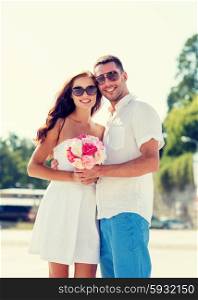 love, wedding, summer, dating and people concept - smiling couple wearing sunglasses standing with bunch of flowers in city