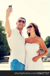 love, wedding, summer, dating and people concept - smiling couple wearing sunglasses hugging and making selfie with smartphone in park
