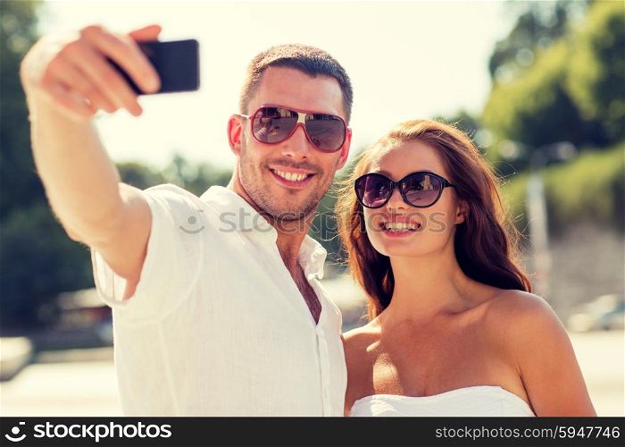 love, wedding, summer, dating and people concept - smiling couple wearing sunglasses hugging and making selfie with smartphone in park