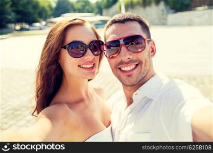 love, wedding, summer, dating and people concept - smiling couple wearing sunglasses making selfie in city