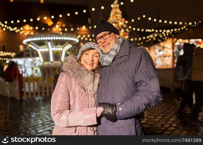 love, winter holidays and people concept - happy senior couple hugging at christmas market on town hall square in tallinn, estonia. happy senior couple hugging at christmas market