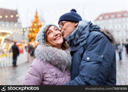 love, winter holidays and people concept - happy senior couple kissing at christmas market on town hall square in tallinn, estonia. happy senior couple kissing at christmas market