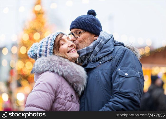 love, winter holidays and people concept - happy senior couple kissing at christmas market. happy senior couple kissing at christmas market