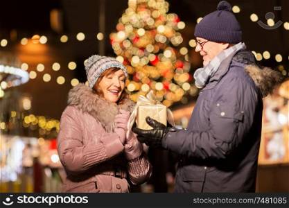 love, winter holidays and people concept - happy senior couple with gift at christmas market on town hall square in tallinn, estonia. happy senior couple with gift at christmas market