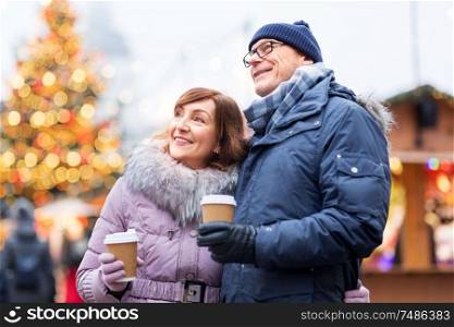 love, winter holidays and people concept - happy senior couple with takeaway coffee at christmas market on town hall square in tallinn, estonia. senior couple with coffee at christmas market