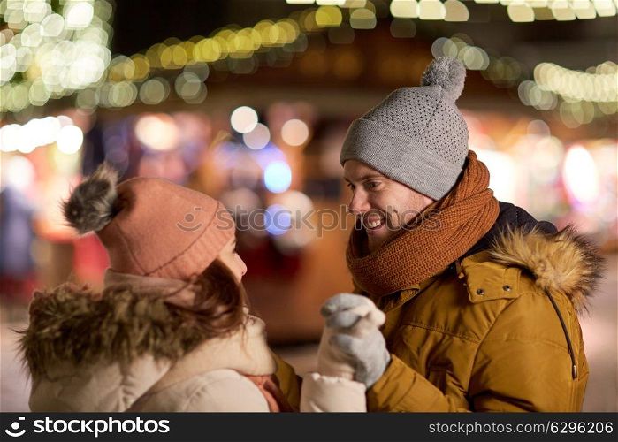 love, winter holidays and people concept - happy young couple dating and holding hands at christmas market in evening. happy couple holding hands at christmas market
