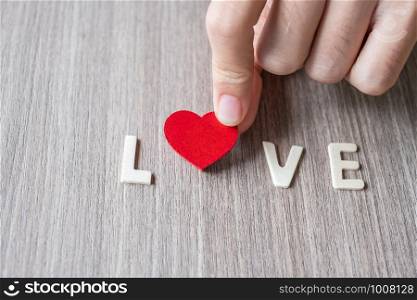 LOVE word of wooden alphabet letters with woman hand holding red heart shape on table background. Romance, Romantic and Valentine's day concepts