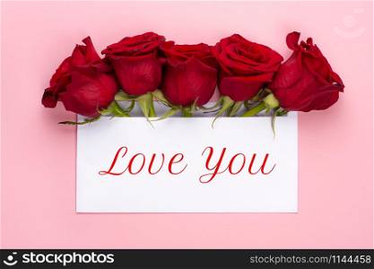 Love you banner. Red rose flowers arrangement with blank card on light pink background. Copy space. Top view. Love you banner. Red rose flowers arrangement with blank card on light pink background.