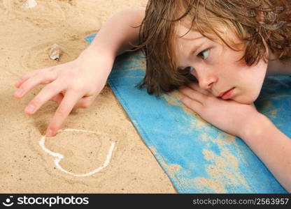 Lovelorn teenage boy lays on the beach drawing a heart in the sand