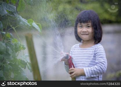lovely asian children pouring water to home garden vegetable plant with happiness face
