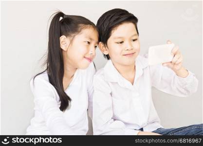 Lovely Asian couple school kids are taking selfie, 7 and 10 years old, over gray background