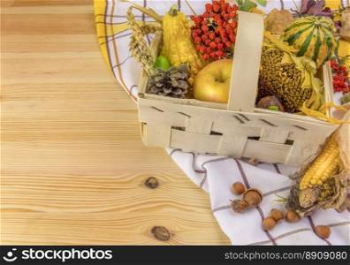 Lovely autumn decoration with all sorts of pumpkins, corn, grain, sunflower and forest fruits, set in a basket, on a towel and a wooden table.