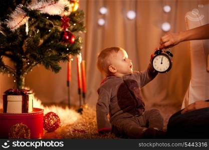 Lovely baby near Christmas tree holding with mother alarm clock&#xA;