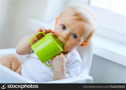 Lovely baby sitting in chair and drinking from baby cup&#xA;