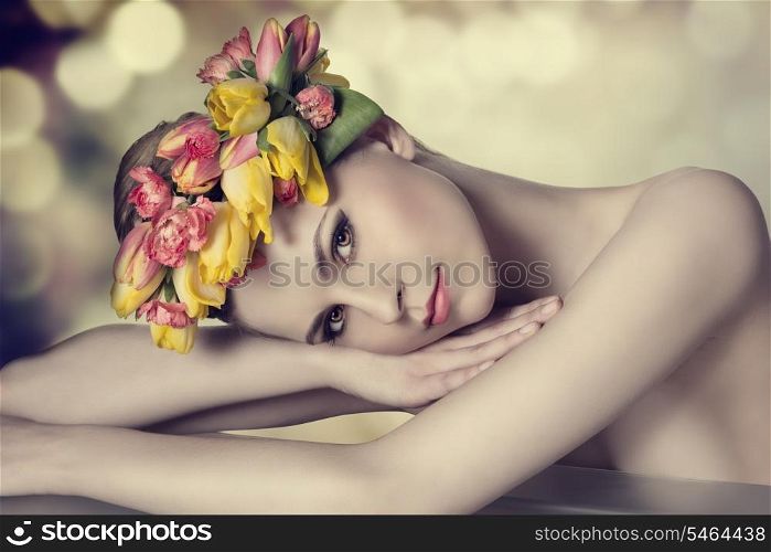 lovely beauty girl with spring floral wreath, colorful make-up, fresh skin and naked shoulders lying on a table and looking in camera with calm expression