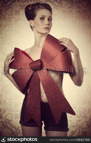 lovely blonde woman adorned like a sensual christmas present with big red bow on her naked breast. Elegant hair-style, looking in camera