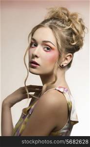 lovely blonde woman with creative hair-style and colored dress posing with brilliant colorful make-up and perfect skin