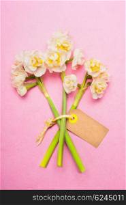Lovely bouquet of daffodils with blank label card on pink background, top view. Spring flowers bunch.