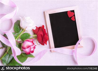 Lovely bouquet of multicolored roses, tied with a pink ribbon, near a blank chalkboard decorated with two red hearts, on a pink background.