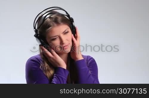 Lovely brunette girl with eyes closed holding both hands on headphones and enjoying beautiful song on mp3 player. Charming young woman opening her eyes, looking at the camera enigmatically and sending air kiss while listening music in earphones.