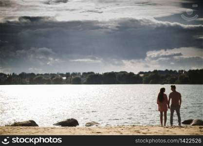 lovely couple stands by the water along river shore, holding hands together, happy family concept. love story.. lovely couple stands by the water along river shore, holding hands together, happy family concept. love story
