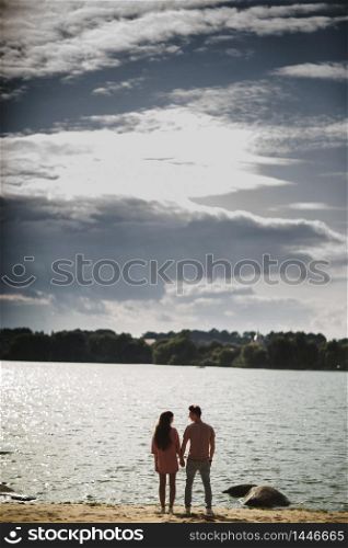 lovely couple stands by the water along river shore, holding hands together, happy family concept. love story.. lovely couple stands by the water along river shore, holding hands together, happy family concept. love story