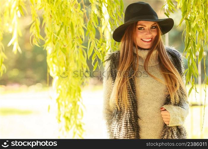 Lovely cute gorgeous woman wearing black hat fur waistcoat sweater posing around leaves of willow tree in park.. Portrait of beauty woman outdoors