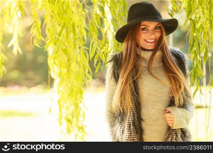 Lovely cute gorgeous woman wearing black hat fur waistcoat sweater posing around leaves of willow tree in park.. Portrait of beauty woman outdoors
