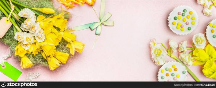 Lovely daffodils flowers, blank label, cake and decorations on pale pastel pink background, top view, banner. Festive spring floral background.
