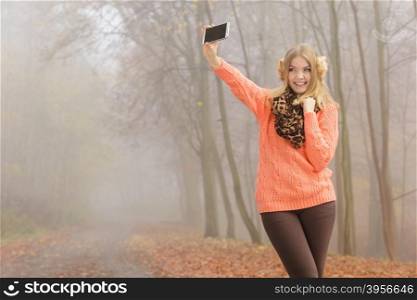 Lovely fashion woman in park taking selfie photo.. Lovely fashion woman in fall autumn park taking selfie self photo picture. Pretty cute young girl in sweater pullover and earmuffs photographing.