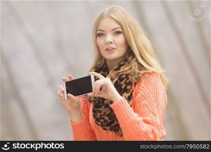Lovely fashion woman in park taking selfie photo.. Lovely fashion woman in fall autumn park taking selfie self photo picture. Pretty cute young girl in sweater pullover photographing.